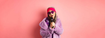 时尚概念时尚的高级亚洲女人唱歌<strong>卡拉ok</strong>执行阶段麦克风穿时尚的太阳镜紫色的人造皮毛外套粉红色的背景