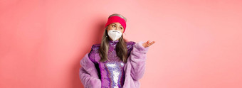 科维德流感大流行时尚概念时尚的亚洲高级女人呼吸器聚会，派对衣服持怀疑态度指出手左站粉红色的背景