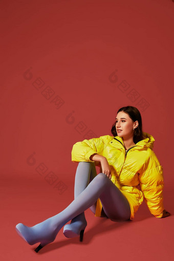 工作室肖像年轻的浅黑肤色的女人女人坐着地板上黄色的夹克灰色蓝色的女裤软管长袜
