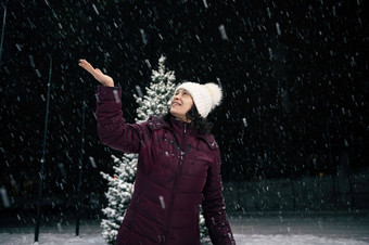 令人愉快的女人捕捉雪花手走城市街雪晚上冬天降雪