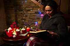 美丽的女人阅读书烛光坐着表格圣诞节礼物花环