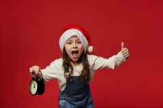 喜出望外孩子女孩穿圣诞老人他显示拇指摆姿势报警时钟显示午夜红色的背景