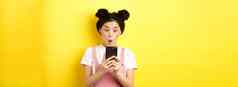 亚洲青少年女孩兴奋智能手机屏幕阅读新闻电话站黄色的背景