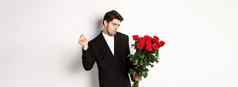 图像优雅的时髦的男人。黑色的西装自信持有花束红色的玫瑰浪漫的日期站白色背景