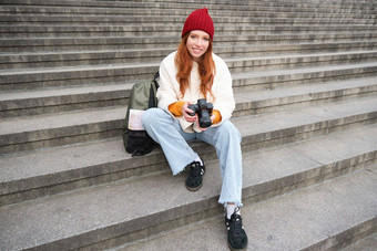 年轻的学生摄影师坐在街楼梯检查照片专业相机采取照片在户外