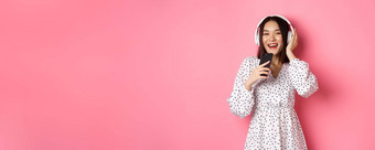 美丽的微笑亚洲女人唱歌首歌智能手机麦克风玩<strong>卡拉ok</strong>应用程序耳机站粉红色的背景