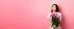 亚洲十几岁的女孩可爱的衣服浪漫的空空间标志持有情人节一天花礼物收到boquet玫瑰情人站粉红色的背景