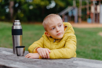 男孩坐着木表格热水瓶杯茶距离男孩坐在表格公园秋天季节孩子男孩儿子秋天公园坐着木板凳上表格孩子在户外