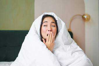 关闭有趣的困了女孩亚洲女人打哈欠醒着的早期早....涵盖了毯子羽绒被持有手打开口