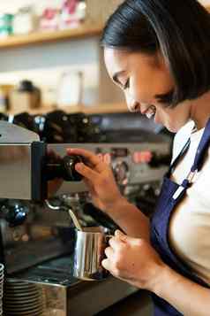 快乐亚洲女人咖啡师咖啡机使订单热气腾腾的牛奶卡布奇诺咖啡拿铁笑微笑工作咖啡馆