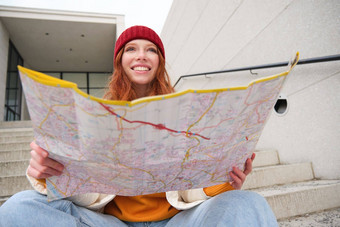 年轻的微笑红色头发的人女孩旅游坐在楼梯在户外城市纸地图方向旅行者背包客探讨了城市观光