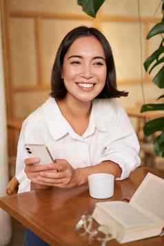 肖像现代女孩坐在咖啡咖啡馆微笑智能手机阅读书餐厅移动电话应用程序