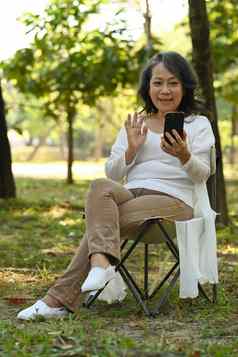 微笑成熟的女人聪明的电话打字消息社会网络坐着折叠椅子公园