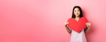 情人节一天概念可爱的十几岁的亚洲女孩显示大红色的心卡下降爱浪漫的日期衣服微笑温柔的相机粉红色的背景