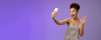 友好的时尚的自信非裔美国人女人银闪闪发光的衣服挥舞着提高了棕榈手势记录视频智能手机问候互联网追随者写博客聚会，派对