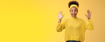 迷人的兴奋微笑友好的千禧非裔美国人女孩提高手隐藏显示手掌高投降站逗乐激动咧着嘴笑有趣的摆姿势黄色的背景