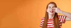 愚蠢的幼稚的红色头发的人女孩傻瓜使小猪鼻子显示舌头不成熟的无忧无虑的有趣的好玩的热情的情绪站乐观的显示鼻孔幸福的咧着嘴笑橙色背景