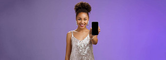 迷人的有吸引力的非裔美国人女人银闪闪发光的时尚的衣服扩展手臂显示智能手机显示展示应用程序促进很酷的设备站很高兴微笑蓝色的背景