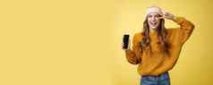 积极的无忧无虑的迷人的年轻的女孩显示和平手势穿《连线》杂志耳机显示智能手机屏幕促进应用程序很酷的品牌移动电话笑无忧无虑的黄色的背景