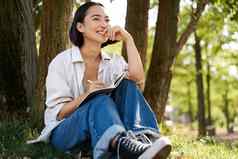 肖像年轻的亚洲女人写作笔记本表达的想法纸日记微笑坐着树夏天一天公园