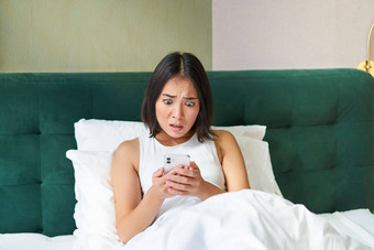 卧室图片亚洲女人说谎床上害怕震惊了智能手机屏幕阅读消息有关脸
