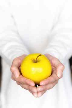 手年轻的女人持有黄色的苹果背景白色毛衣新鲜的水果柔和的颜色特写镜头前视图