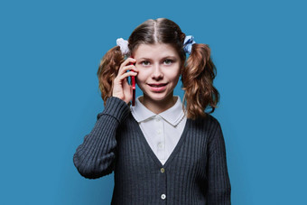 微笑13岁以下的女学生会说话的移动电话蓝色的工作室背景