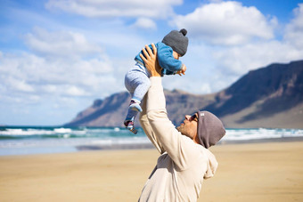 父亲享受纯自然持有玩婴儿婴儿男孩太阳多风的桑迪海滩法马拉兰斯洛特岛西班牙家庭旅行育儿概念