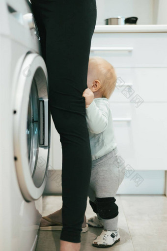 婴儿婴儿男孩孩子隐藏母亲腿要求注意多任务处理家庭家务厨房首页妈妈。孕妇离开