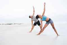 拉伸变革年轻的男人。女人练习瑜伽海滩