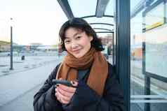 美丽的年轻的女人站公共汽车停止等待公共运输移动电话智能手机应用程序