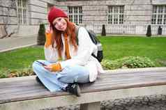 肖像时尚的年轻的女人年坐在板凳上公园移动电话读取在线新闻消息手表视频智能手机应用程序连接公共无线网络