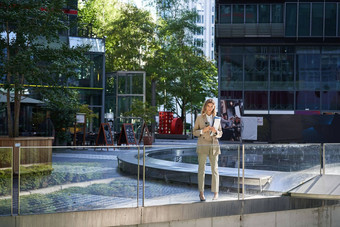 企业女人西装站信心米色西装工作文档在户外摆姿势城市中心