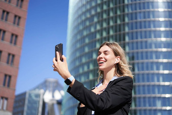 肖像微笑企业女人视频调用街持有移动电话挥舞着智能手机相机穿西装
