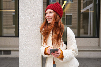 美丽的红色头发的人女孩智能手机站街持有移动电话出租车应用程序连接公共无线网络互联网发送文本消息