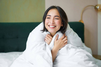 可爱的温柔的女人坐着床上温暖的羽绒被微笑窗口享受早....安慰毯子