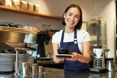 肖像美丽的亚洲女孩学生工作兼职咖啡馆持有杯咖啡使订单客户端穿统一的