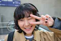 头肖像朝鲜文女孩站街显示和平标志穿耳机听音乐微笑