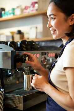 快乐亚洲女人咖啡师咖啡机使订单热气腾腾的牛奶卡布奇诺咖啡拿铁笑微笑工作咖啡馆