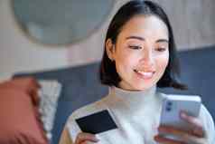 肖像微笑亚洲女人支付信贷卡智能手机应用程序安排直接借记购物在线移动电话