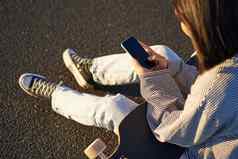 关闭溜冰者青少年女孩坐在滑板类型消息智能手机移动电话屏幕