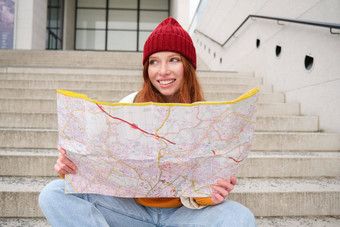 年轻的微笑红色头发的人女孩旅游坐在楼梯在户外城市纸地图方向旅行者背包客探讨了城市观光