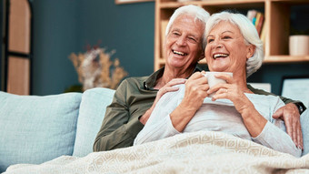 爱高级夫妇放松沙发喝咖啡看喜剧电影电视退休男人。女人沙发上生活房间看微笑感情首页