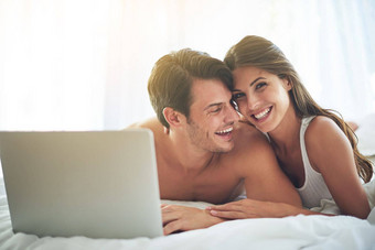 移动PC快乐夫妇说谎床上看在线电影视频首页幸福微笑肖像女人浏览互联网电脑丈夫卧室