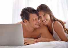 移动PC爱快乐夫妇说谎床上看在线电影视频首页幸福微笑肖像女人浏览互联网电脑丈夫卧室