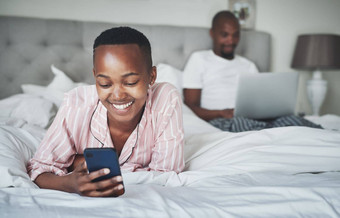 黑色的女人智能手机放松床上技术在线沟通网站无线网络男人。移动PC夫妇快乐首页科技社会媒体互联网连接应用程序