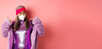 科维德流感大流行时尚概念时尚亚洲祖母穿闪闪发光的聚会，派对衣服呼吸器指出面具粉红色的背景