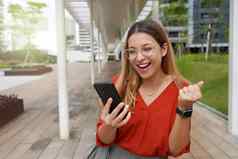 美丽的成功的巴西女兴奋提高了手欢乐智能手机年轻的女人看移动电话庆祝好新闻工作早....