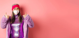 科维德流感大<strong>流行时尚</strong>概念快乐的亚洲高级女人聚会冠状病毒呼吸器显示竖起大拇指推荐穿脸面具粉红色的背景