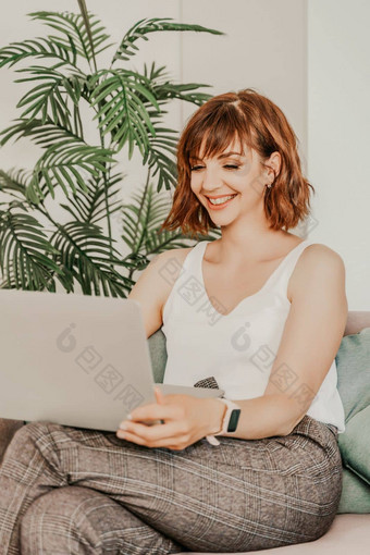 浅黑肤色的女人苹果笔记本电脑沙发有吸引力的年轻的女人工作移动PC坐着沙发上首页穿光上衣裤子